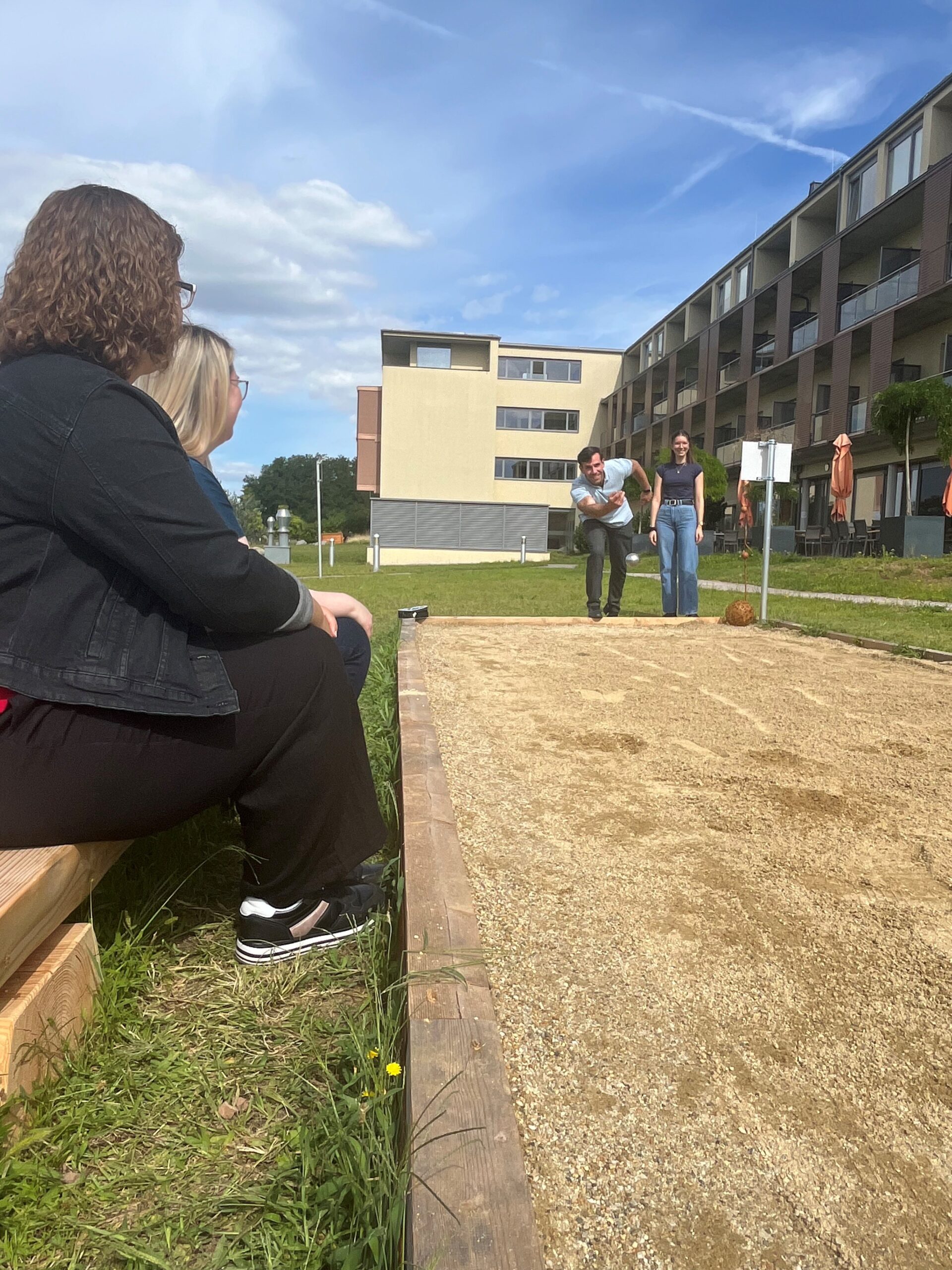 Zwei Personen spielen Boccia und zwei schauen dabei zu. Im Hintergrund ist die Privatklinik Hollenburg zu sehen.