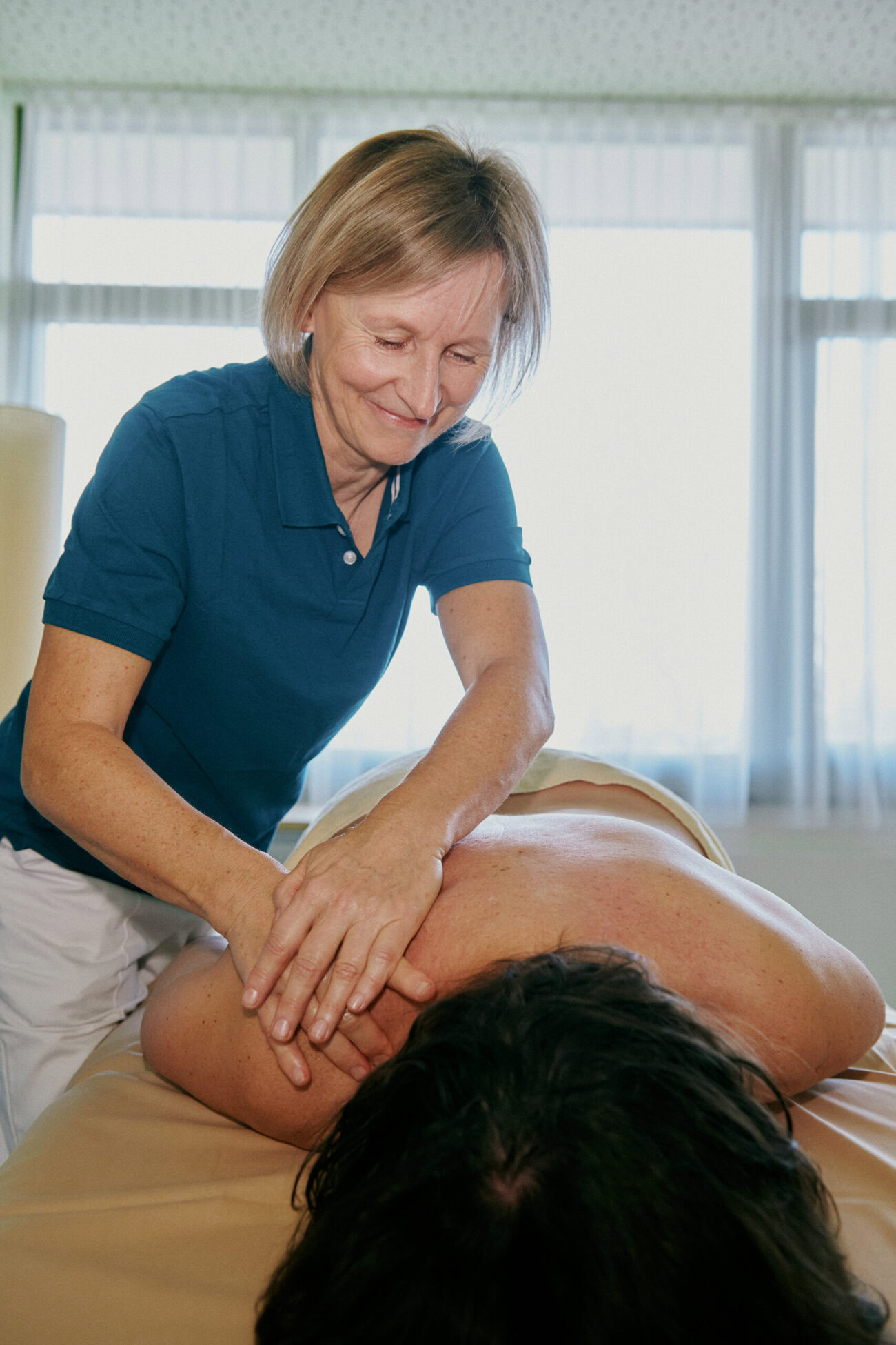 Eine Masseurin massiert einen Mann, der auf einem Massagetisch liegt.