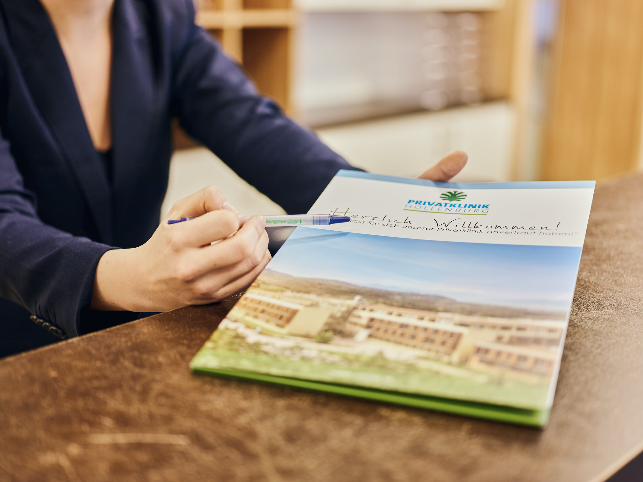Foto einer Broschüre der Privatklinik Hollenbrunn. Eine Hand zeigt mit einem Kugelschreiber auf den Text Herzlich Willkommen.
