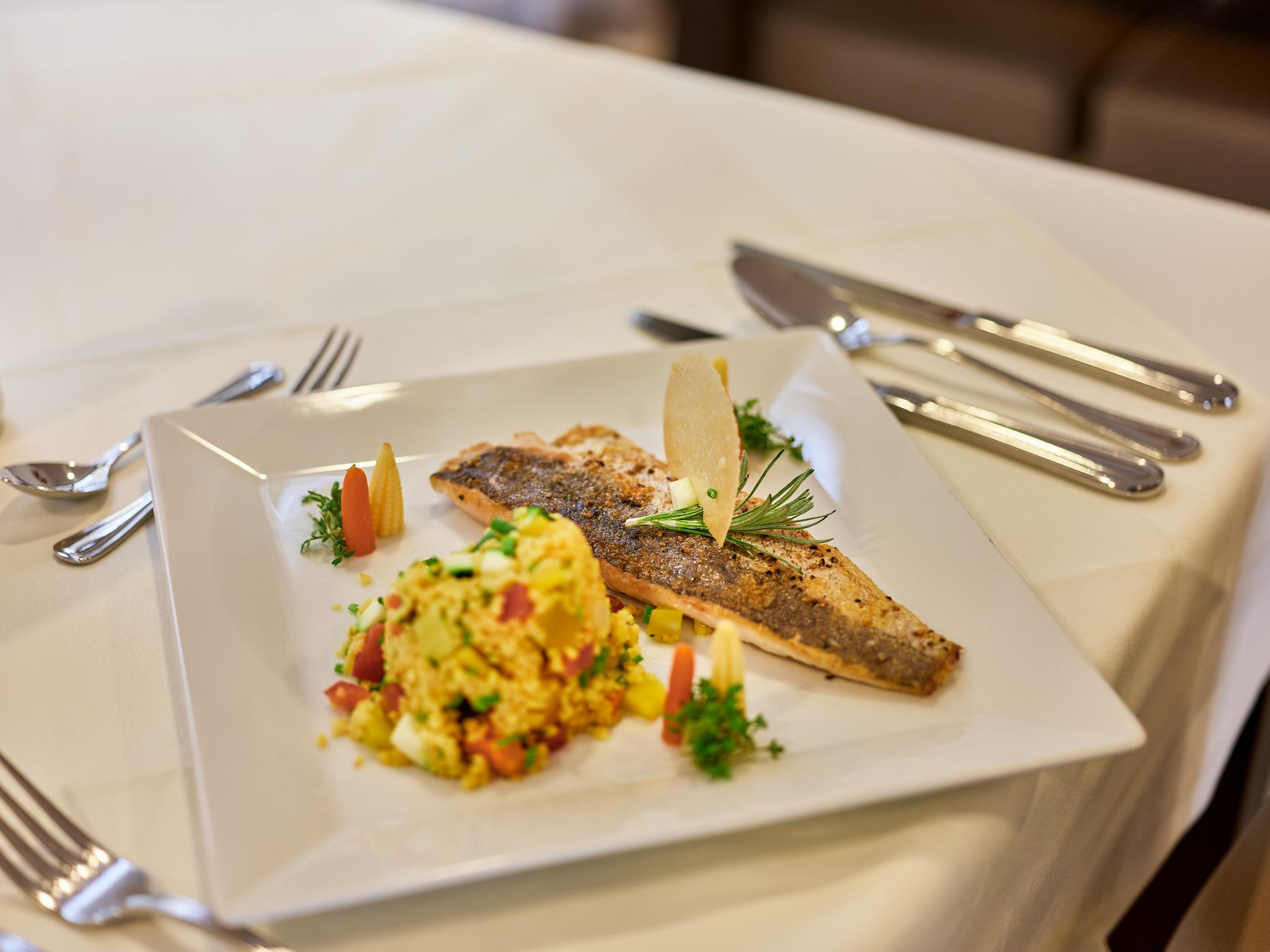Ein eckiger Teller mit Fisch und einer Beilage aus Gemüse und Couscous.